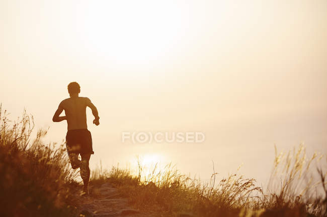 Man running on trail overlooking sunset ocean — Stock Photo