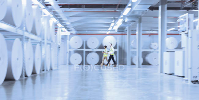 Travailleurs marchant le long de grandes bobines de papier dans l'usine d'impression — Photo de stock