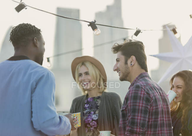 Amigos adultos jóvenes hablando y bebiendo en la fiesta en la azotea - foto de stock