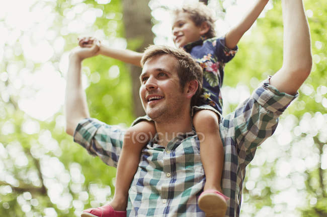 Father carrying son on shoulders below trees — Stock Photo