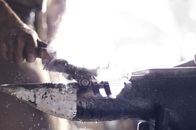 Primer plano de herrero cepillando herramienta de hierro sobre yunque en forja - foto de stock