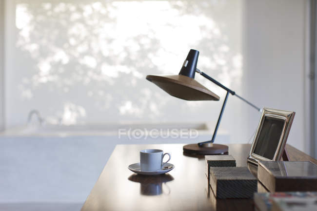 Cup of coffee and lamp on desk in office — Stock Photo