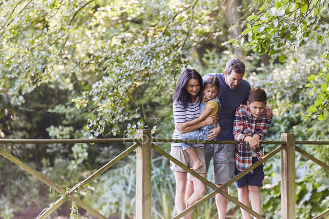 Family standing on footbridge in park with trees — Stock Photo