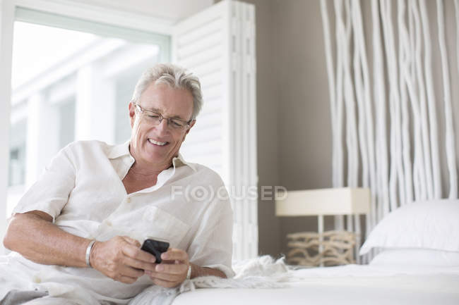 Літня людина, за допомогою мобільного телефону на ліжку — стокове фото