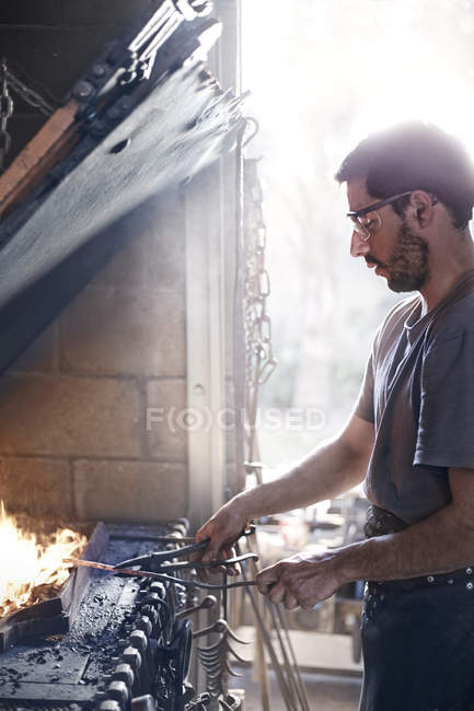 Blacksmith working over fire in forge — Stock Photo
