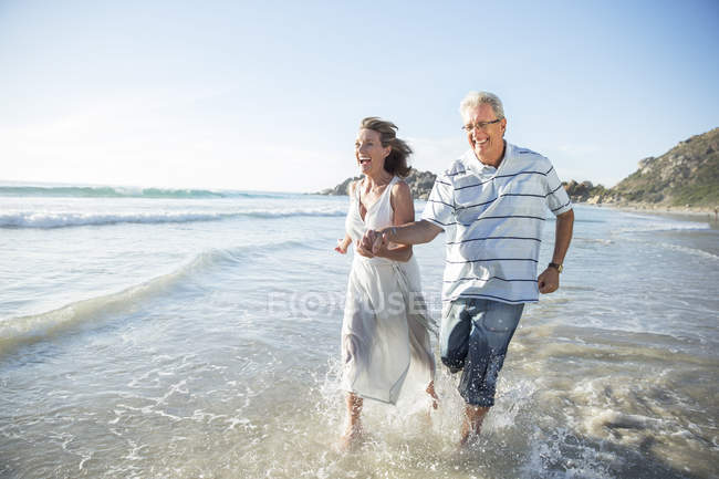 Coppia più anziana che gioca sulle onde sulla spiaggia — Foto stock