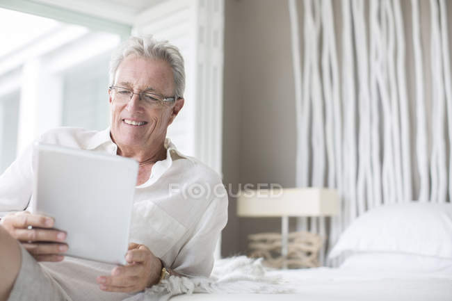 Uomo più anziano utilizzando tablet digitale sul letto — Foto stock