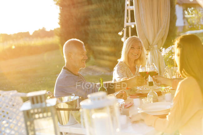 Casal sênior uma filha adulta brindar copos de vinho na mesa do pátio ensolarado — Fotografia de Stock