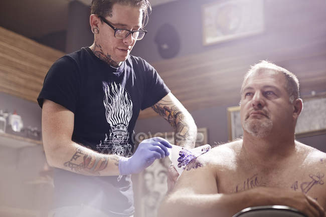 Tattoo artist tattooing man shoulder at studio — Stock Photo