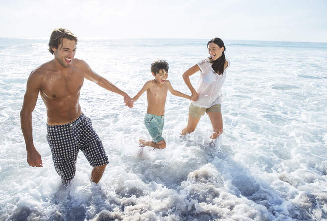 Famille jouant dans les vagues à la plage — Photo de stock