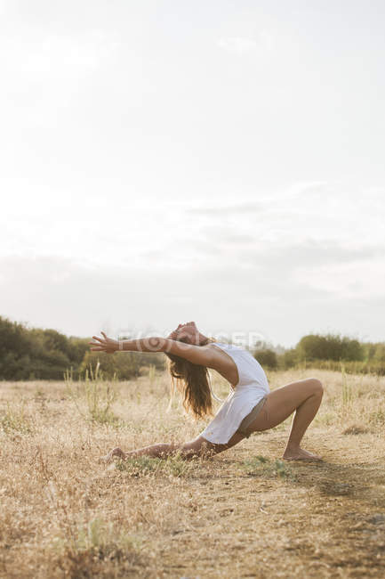 Boho woman in high crescent lunge yoga pose in sunny rural field — Stock Photo