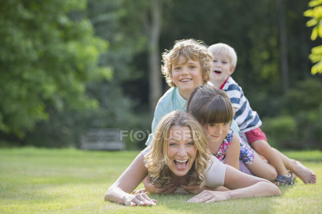 Happy children laying on mother in grass — Stock Photo