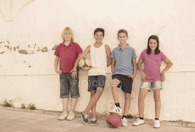 Діти з футбольними м'ячами спираються на стіну — стокове фото