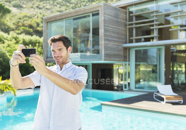 Homem tomando auto-retrato com telefone câmera na beira da piscina — Fotografia de Stock