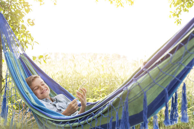 Carefree boy listening to music on mp3 player in rural hammock — Stock Photo