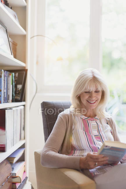 Sorrindo sênior mulher ler livro em den — Fotografia de Stock
