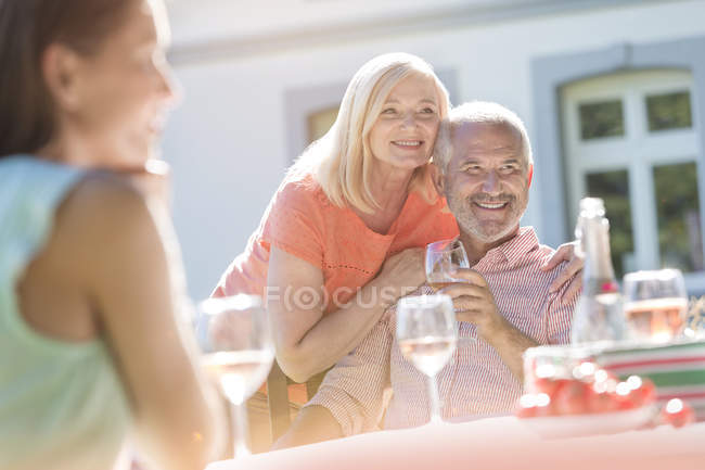 Seniorenpaar lächelt und trinkt Wein auf sonniger Terrasse — Stockfoto
