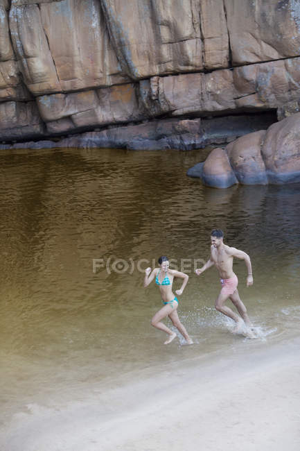 Casal correndo no lago contra rocha — Fotografia de Stock