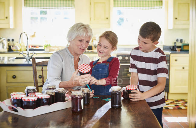Бабушка консервирует варенье с внуками на кухне — стоковое фото