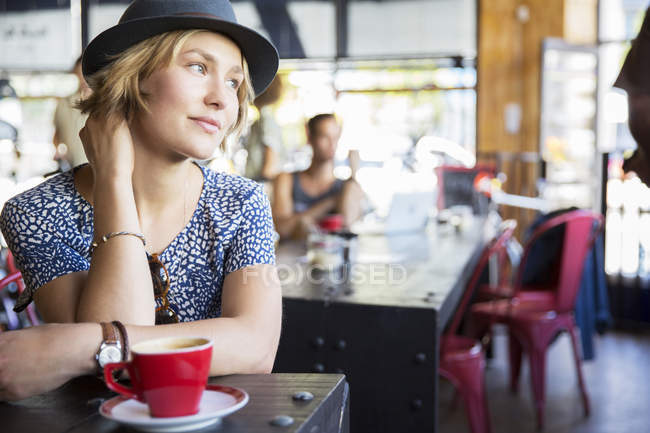 Pensive woman in hat with coffee looking away in cafe — Stock Photo