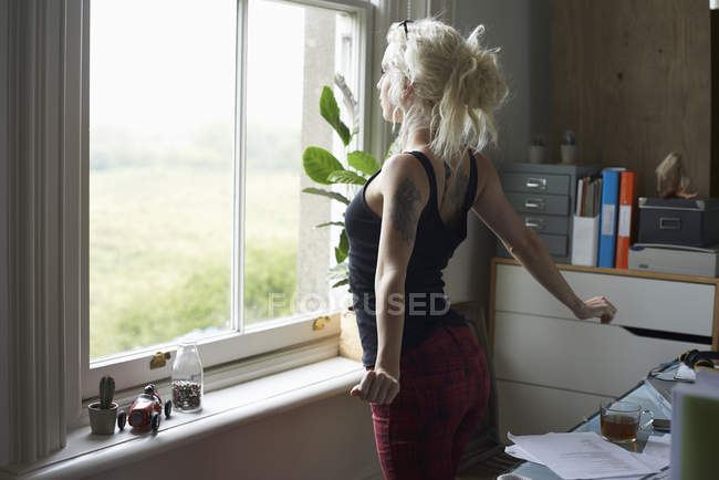 Junge Frau streckt sich am Fenster im Home Office — Stockfoto