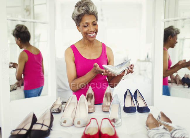 Улыбающаяся зрелая женщина, смотрящая на высокие каблуки в шкафу — стоковое фото