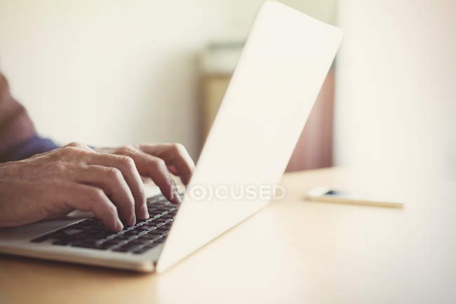 Старший чоловік друкує на ноутбуці за столом — стокове фото