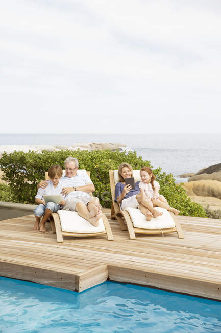 Older couple and grandchildren relaxing by pool — Stock Photo