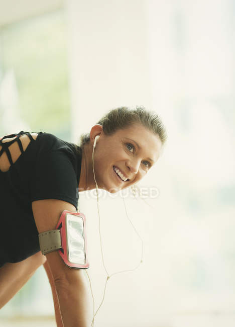 Mujer sonriente con auriculares y brazalete reproductor de mp3 en el gimnasio - foto de stock