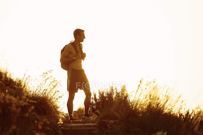 Bare chested male hiker with backpack on trail at sunset — Stock Photo