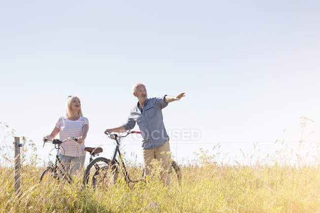 Senior couple bike riding in sunny rural field under blue sky — Stock Photo