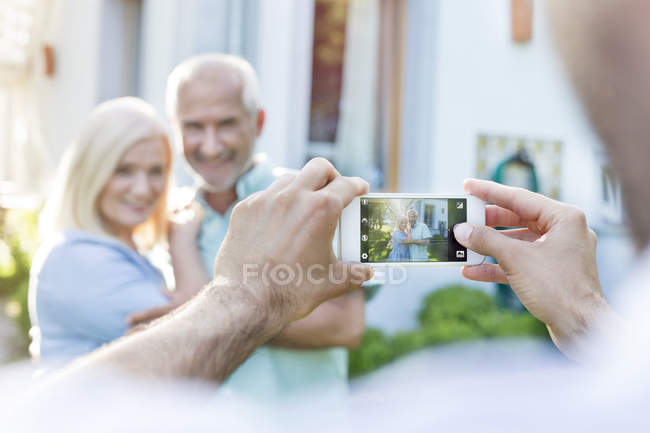 Мужчина фотографирует пожилую пару с камерой телефона — стоковое фото