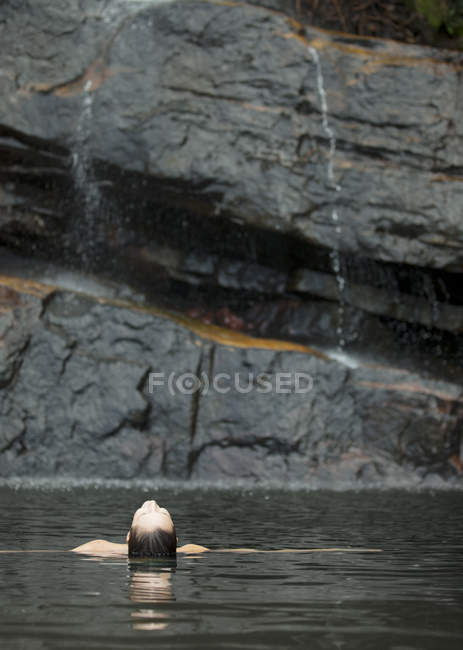 Mulher nadando na piscina contra a rocha — Fotografia de Stock