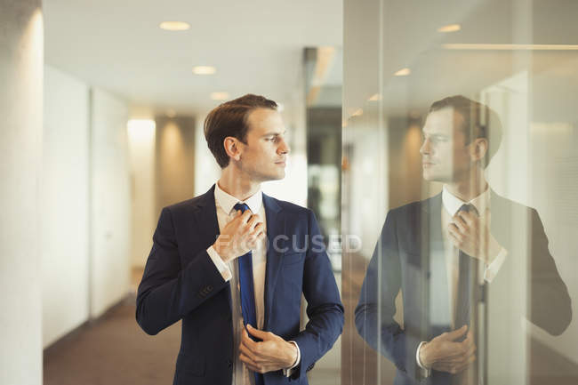 Confident businessman adjusting tie in office corridor — Stock Photo