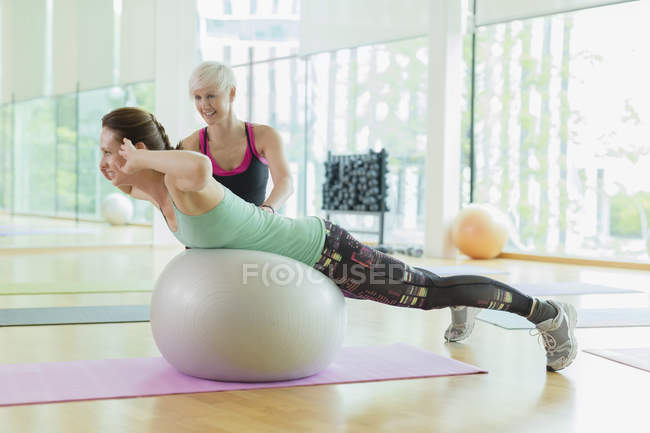 Personal trainer guiding woman doing back extensions on fitness ball — Stock Photo
