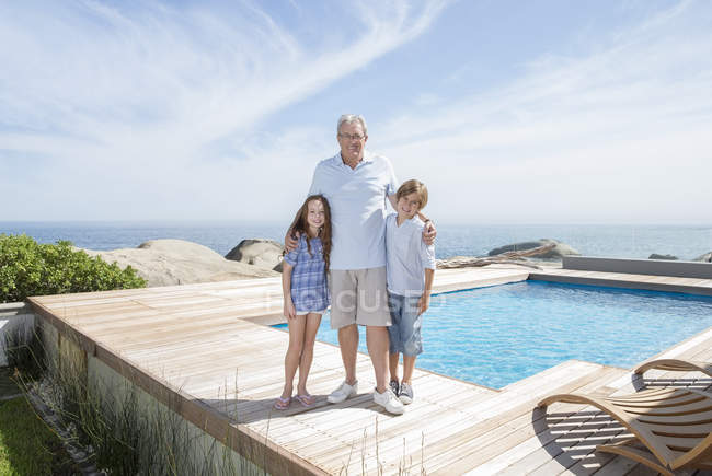 Hombre mayor y nietos sonriendo junto a la piscina - foto de stock
