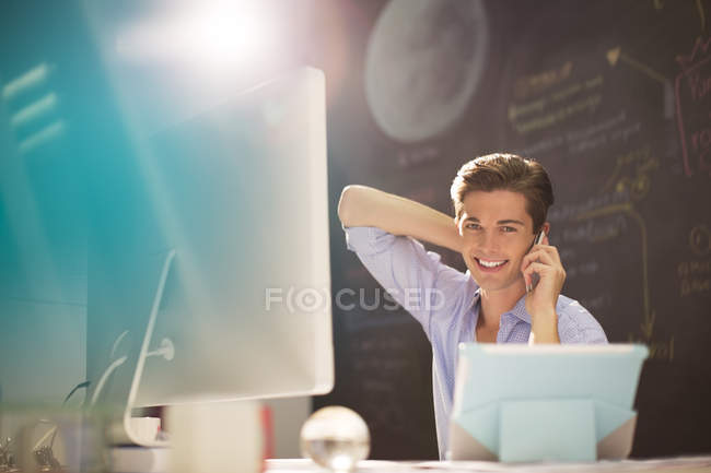 Businessman talking on cell phone at desk in office — Stock Photo