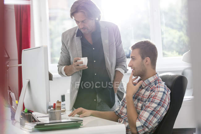 Бізнесмени п'ють каву і працюють за комп'ютером в офісі — стокове фото