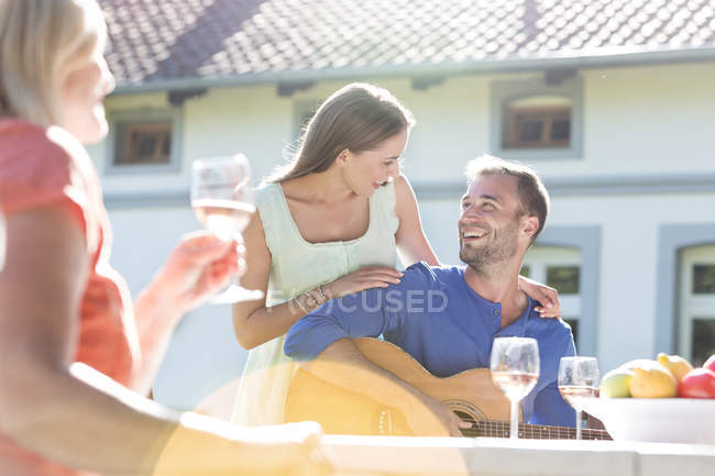Lächelndes junges Paar spielt Gitarre und trinkt Wein auf sonniger Terrasse — Stockfoto