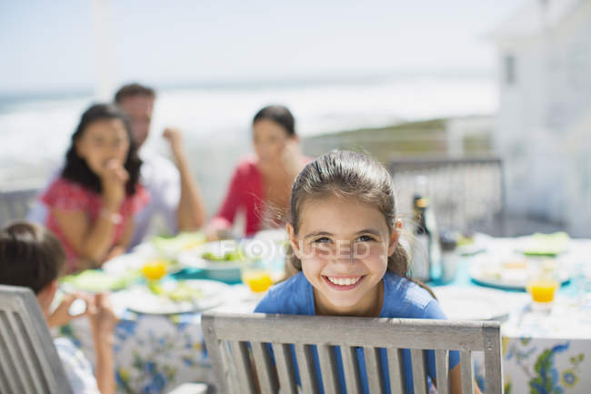 Menina sorridente à mesa no pátio ensolarado — Fotografia de Stock