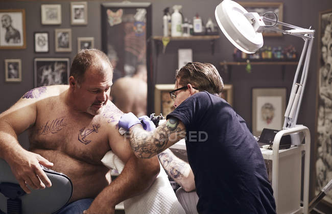 Татуировщик татуирует мужское плечо в студии — стоковое фото