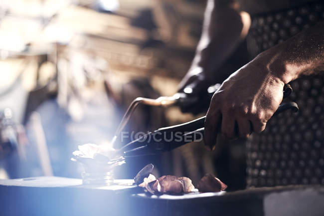 Close up of blacksmith heating metal with blowtorch in forge — Stock Photo