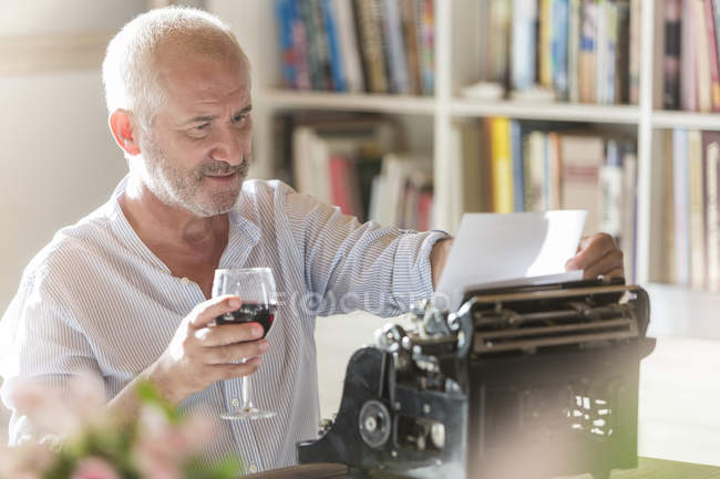 Senior man drinking wine at typewriter in study — Stock Photo