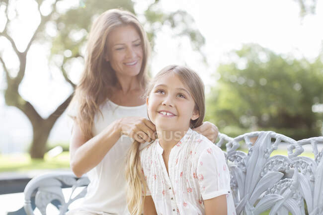 Mother braiding daughter's hair outdoors — Stock Photo