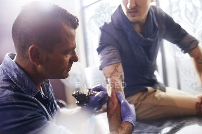 Татуировщик татуирует человека на предплечье в студии — стоковое фото