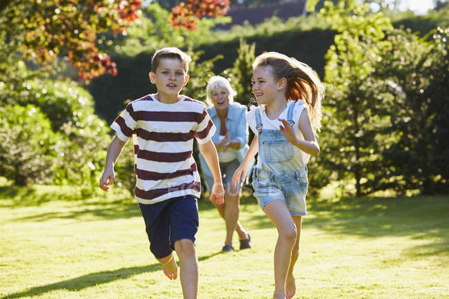 Fratello e sorella che corrono nel giardino soleggiato — Foto stock