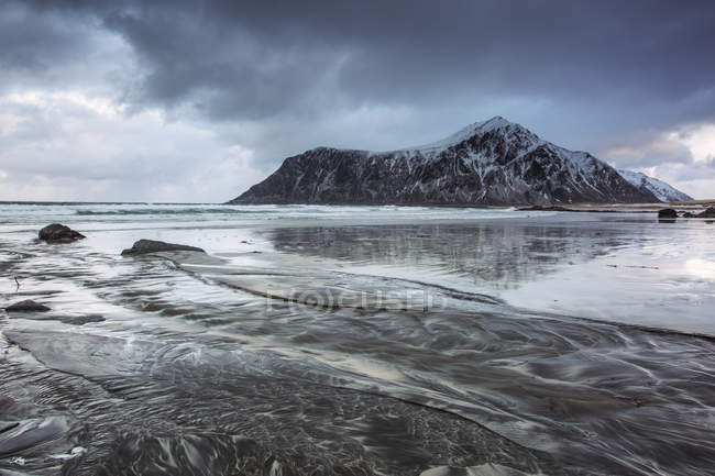 Formación rocosa cubierta de nieve en la playa del océano frío, Skagsanden Beach, Islas Lofoten, Noruega - foto de stock