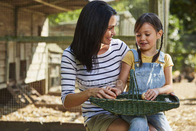 Mother and daughter with basket of eggs outside chicken coop — Stock Photo