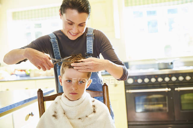 Infelice ragazzo ottenere taglio di capelli da madre in cucina — Foto stock