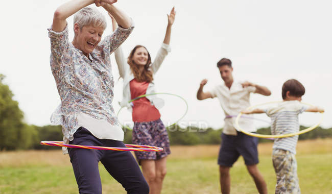 Playful multi-generation family spinning in plastic hoops in field — Stock Photo